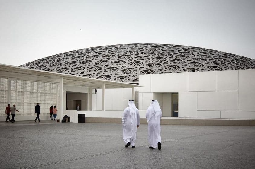 Touristen im Louvre Abu Dhabi Museum und zwei Personen in traditioneller weißer Emirati Kleidung.