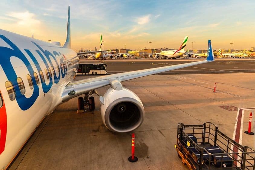 Flydubai-Flugzeug geparkt mit mehreren anderen Flugzeugen im Hintergrund und einem Passagiertransportbus, rechts mit Gepäck auf einem kleinen Transportfahrzeug.