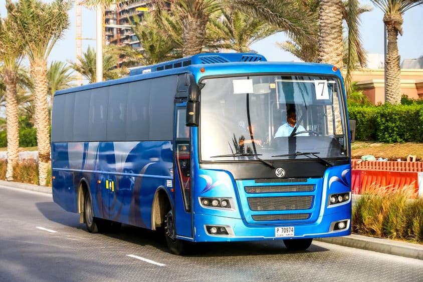 Blauer Bus in Dubai mit Palmen im Hintergrund.
