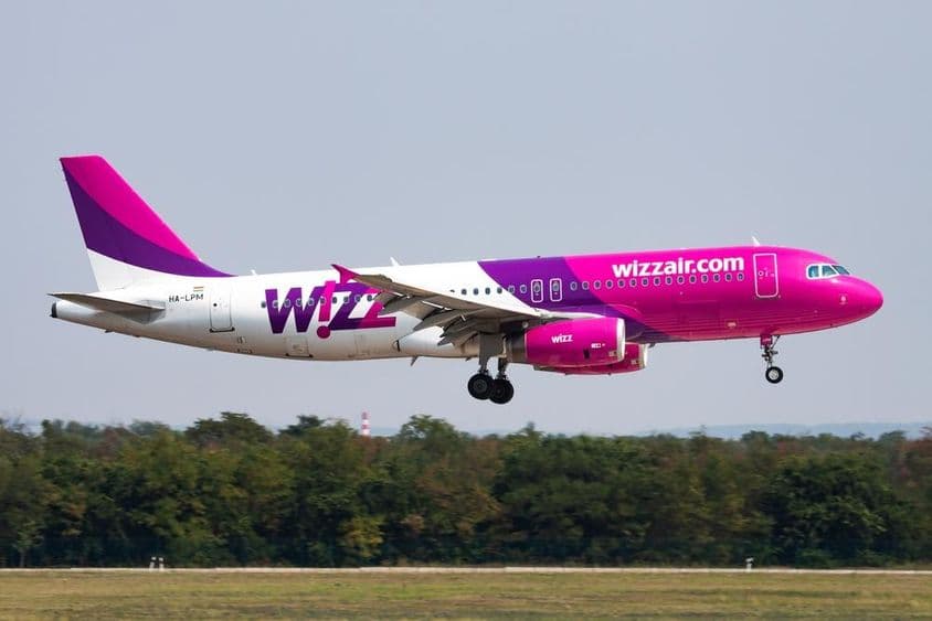 Wizz-Air-Flugzeug fliegt in geringer Höhe mit einem Wald im Hintergrund.