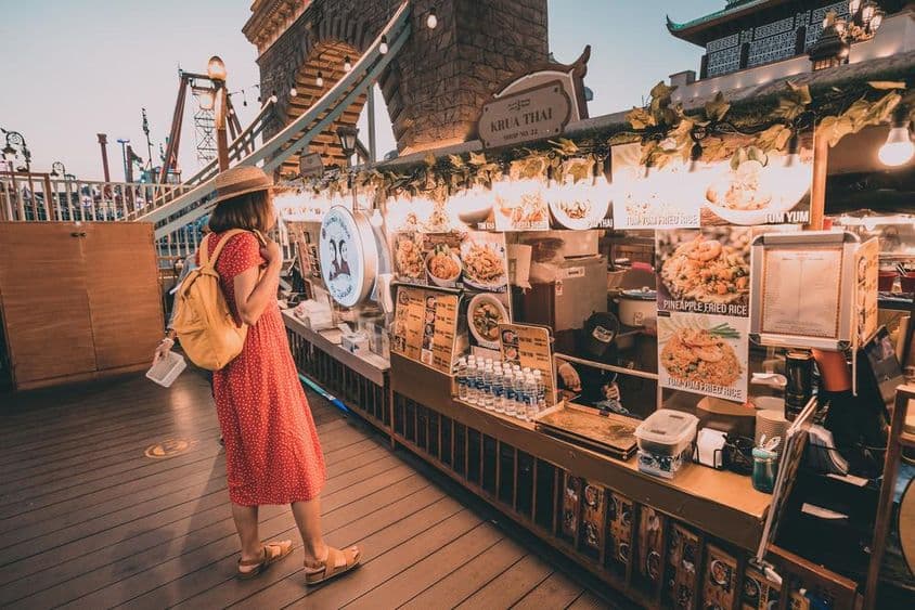 Frau in rotem Tupfenkleid betrachtet nationale Küchen im Global Village Dubai.