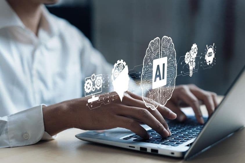 Projektion über ein Notebook, das ein KI-Gehirn und andere Elemente zeigt. Eine menschliche Hand arbeitet am Computer.