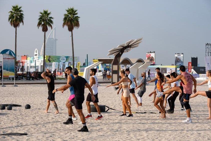 Eine Gruppe von Menschen, die während der Dubai Fitness Challenge auf einem Sandstrand trainiert.
