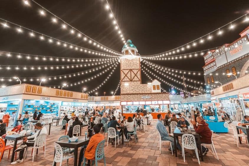Global Village, Touristen und Einheimische probieren Essensspezialitäten an Tischen.