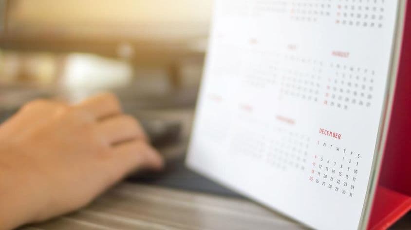 Eine Hand neben einem Kalender, mit verschwommenen Monaten, Dezember klar sichtbar.