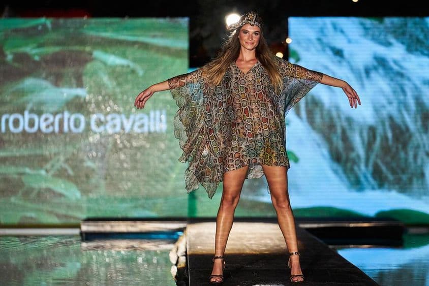 Roberto Cavalli-Zeichen im Hintergrund zu sehen, im Vordergrund eine weibliche Figur in einem Roberto Cavalli-Kleid auf dem Laufsteg.
