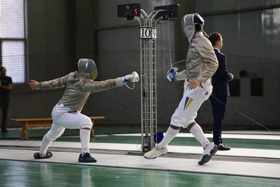 Zwei Fechter im Duell auf der Planche, einer erzielt einen Treffer.