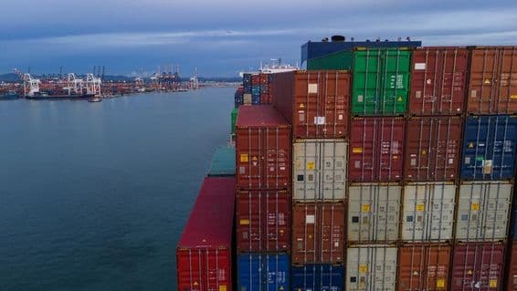 Links ist eine Bucht eines Seehafens sichtbar, rechts gestapelte Container.