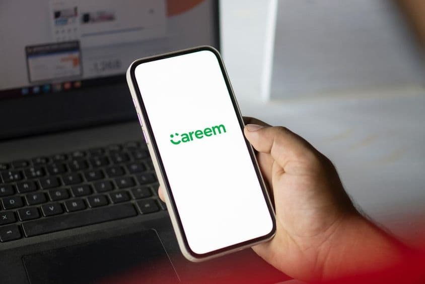 Eine Hand hält ein Handy mit laufender Careem-App und ein Notizbuch ist im Hintergrund sichtbar.