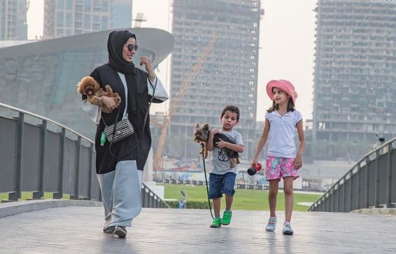 Eine Familie zu viert vor Dubais Wolkenkratzern, wobei die Mutter und ein Kind einen Hund halten.