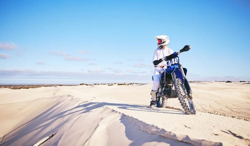 Person fährt Motorrad in der Wüste, trägt weiße Kleidung auf einem blauen Motorrad.