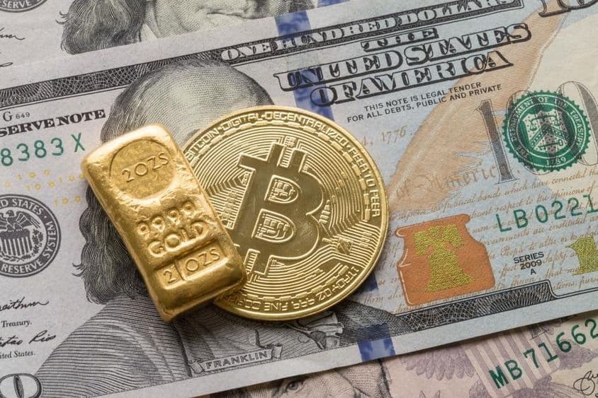 Eine Investitionsgoldbarren und eine Bitcoin-Münze über einem 100-Dollar-Schein.