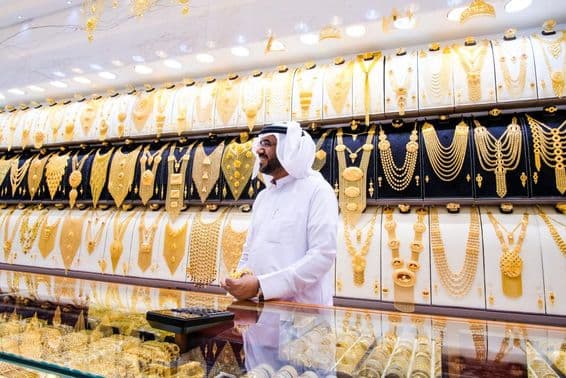 Dubaier Goldverkäufer, mit einem Hintergrund aus vielen Goldketten, der Verkäufer in traditioneller weißer Kleidung.