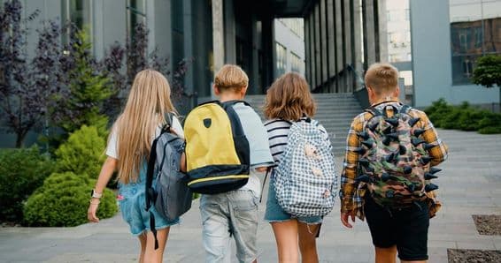 Schüler tragen Rucksäcke vor einem Schuleingang.