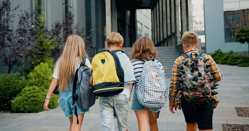 Schüler tragen Rucksäcke vor einem Schuleingang.