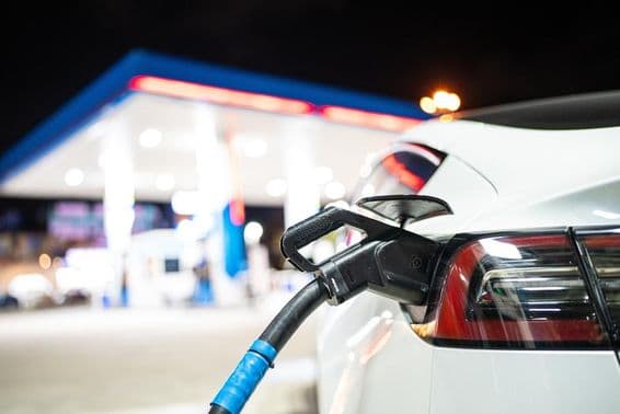 Ein Tesla wird aufgeladen, mit einer Tankstelle im Hintergrund.