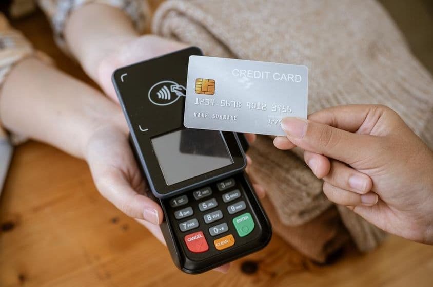 Eine Bankkarte, die von einer Hand gehalten wird, mit einem Kartenlesegerät im Hintergrund.