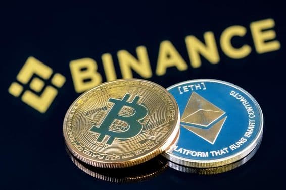 Binance-Inschrift im Hintergrund auf einem schwarzen Tisch mit einer Bitcoin- und einer Ethereum-Münze.
