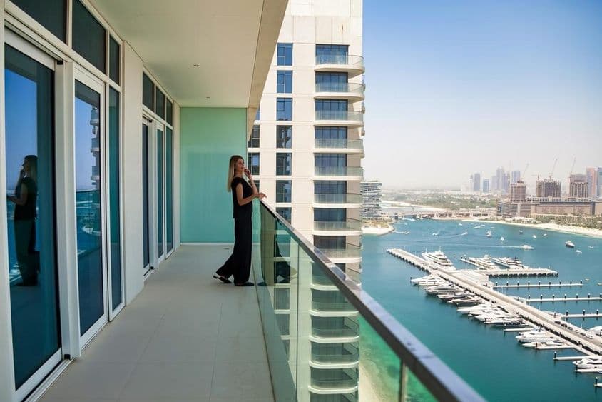 Eine Frau auf einer Terrasse in Dubai beobachtet Boote auf dem Kanal mit einem Wolkenkratzer im Hintergrund.