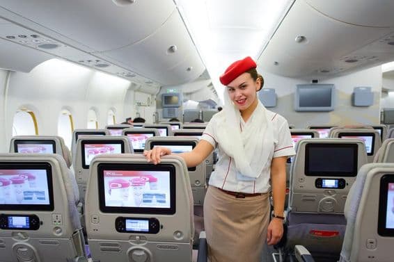 Innenraum eines Emirates-Flugzeugs mit einer Flugbegleiterin im Vordergrund.