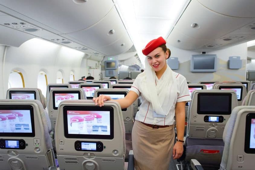 Innenraum eines Emirates-Flugzeugs mit einer Flugbegleiterin im Vordergrund.