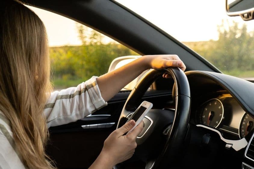 Eine Frau benutzt während des Fahrens ein Mobiltelefon und hält das Lenkrad mit der anderen Hand.