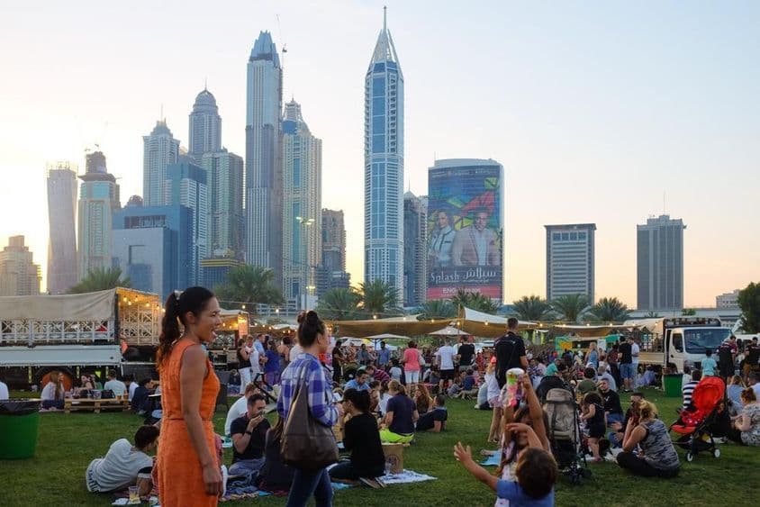 Menschen in Dubai sitzen in einem Park, Wolkenkratzer im Hintergrund.