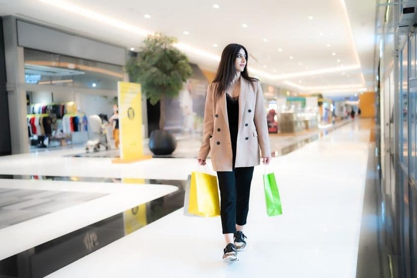 Eine Frau, die in der Dubai Mall einkauft, mit zwei Taschen in der Hand und Geschäften im Hintergrund.
