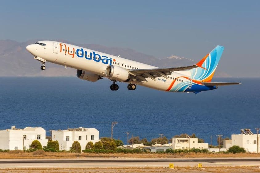 Flydubai-Flugzeug fliegt in niedriger Höhe, mit kleinen weißen Häusern und dem Meer im Hintergrund.