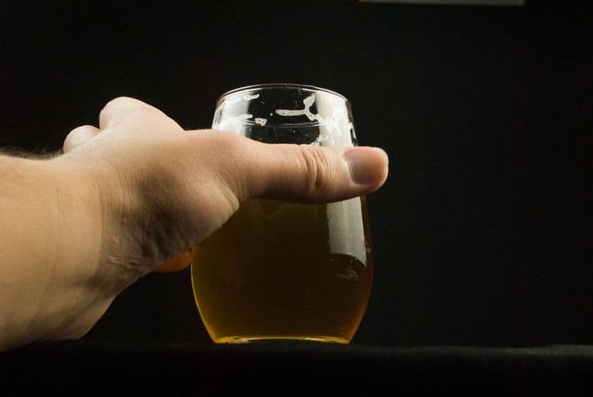 Eine Hand, die ein Bierglas hält, nur die Hand und das Glas sind sichtbar.