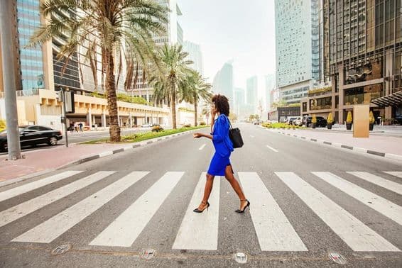 In Dubai überquert eine Frau einen Zebrastreifen auf einer leeren Straße, mit Häusern im Hintergrund sichtbar.