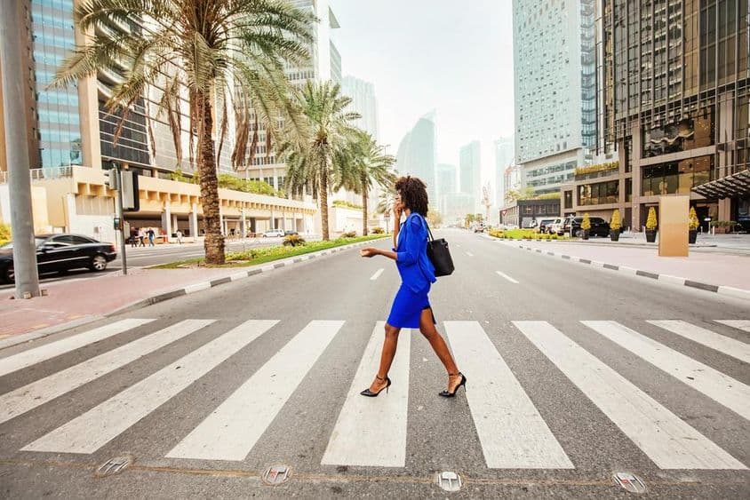 In Dubai überquert eine Frau einen Zebrastreifen auf einer leeren Straße, mit Häusern im Hintergrund sichtbar.