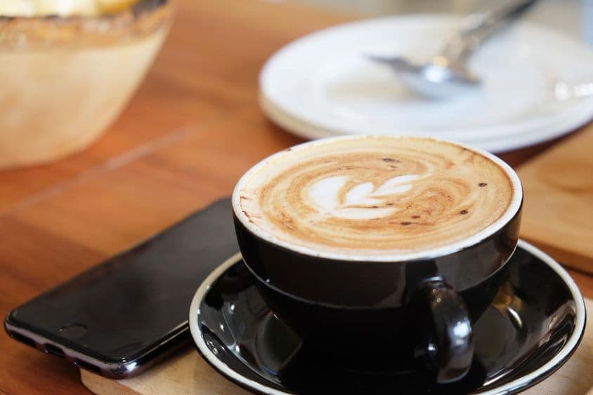 Eine Tasse Cappuccino auf einem Tisch mit einem danebenliegenden Telefon.