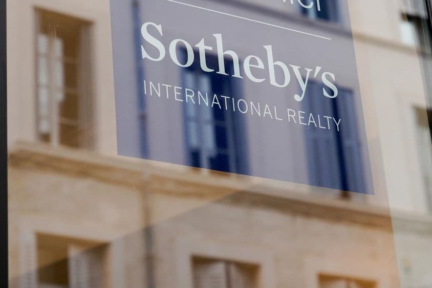 Sotheby’s-Schild sichtbar an der Front eines Gebäudes, auf einer transparenten Tafel.