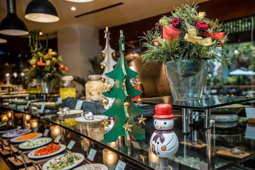 Kleiner Schneemann in einem Restaurant auf einem Gemüsetresen, neben einem hölzernen Weihnachtsbaum.