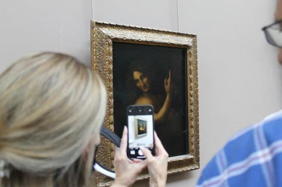 Das Gemälde Johannes der Täufer an einer Wand mit einer Frau, die ein Foto davon mit einem Handy macht.