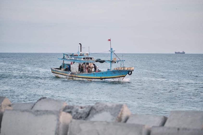 Ein verwittertes Fischerboot mit Menschen an Bord auf dem Meer.