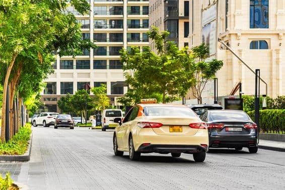 Autos auf Dubais Straßen, ein Taxi im Vordergrund, Häuser im Hintergrund.