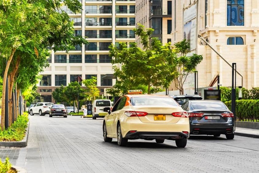 Autos auf Dubais Straßen, ein Taxi im Vordergrund, Häuser im Hintergrund.
