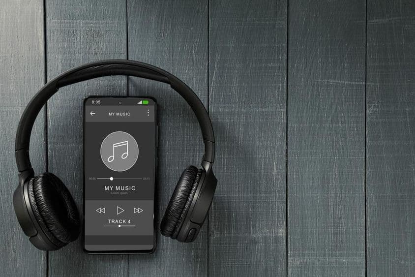 Musikwiedergabe läuft auf einem Telefon, mit Kopfhörern daneben.