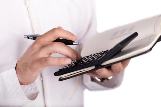 Taschenrechner auf Notizblock, der von einer Hand bedient wird.