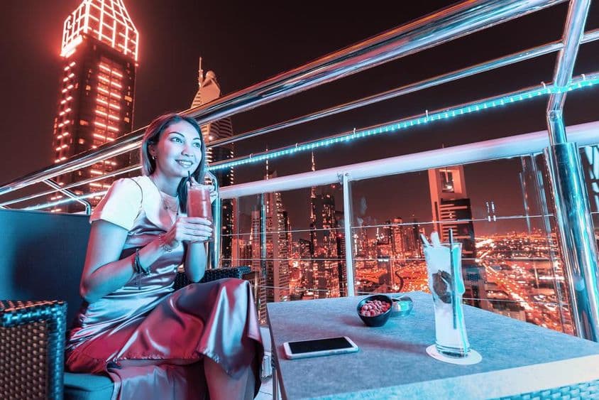Junge Frau genießt Cocktails auf einer Dachterrassenbar in Dubai.