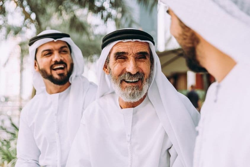 Ein älterer Emirati-Mann spricht mit zwei jüngeren Personen.