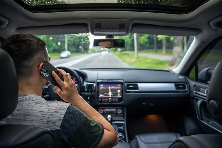 Junger Mann benutzt sein Handy beim Autofahren.