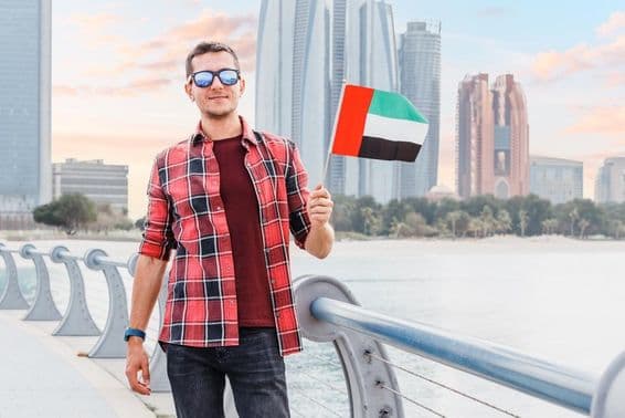 Junger Mann in Dubai Marina, der eine Flagge der VAE hält.