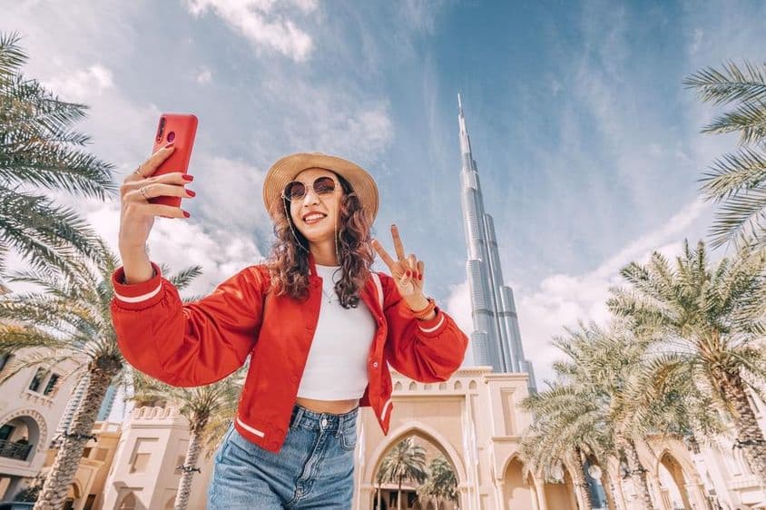 Junge Frau, in rotem Oberteil, macht ein Selfie mit dem Burj Khalifa im Hintergrund.