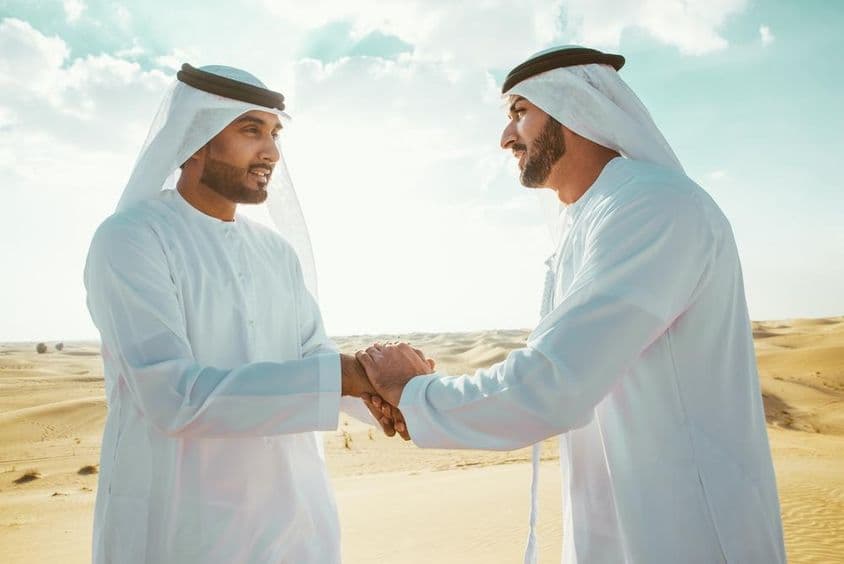 Zwei arabische Männer schütteln sich in der Wüste die Hände.