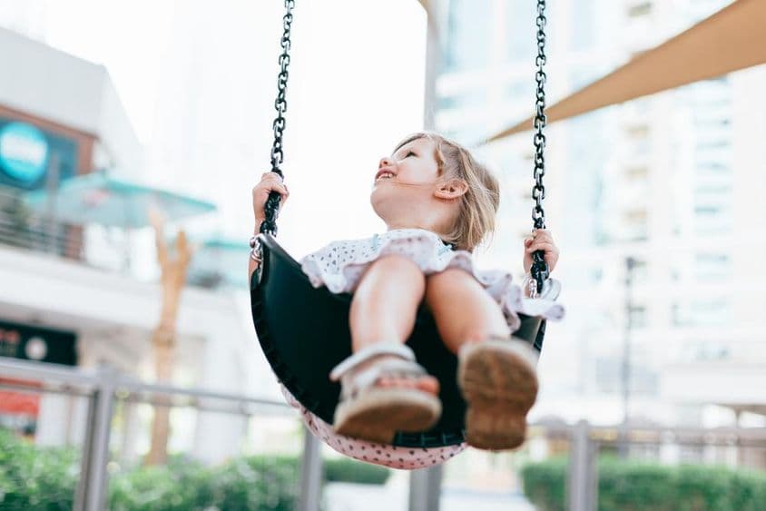 Fröhliches kleines Mädchen schaukelt im Kindergartenhof.