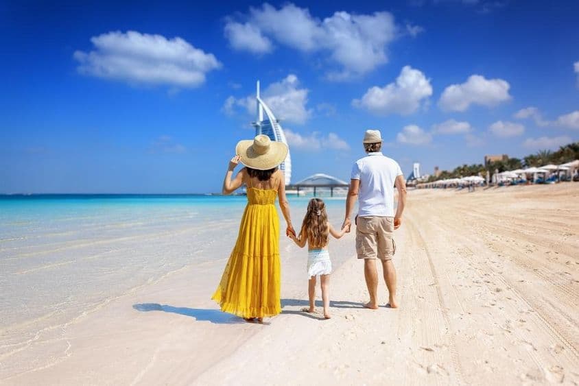 Eine Familie spaziert am Strand von Dubai mit dem Burj al Arab im Hintergrund.