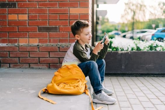 Junge nutzt ein Handy auf Schultreppen.